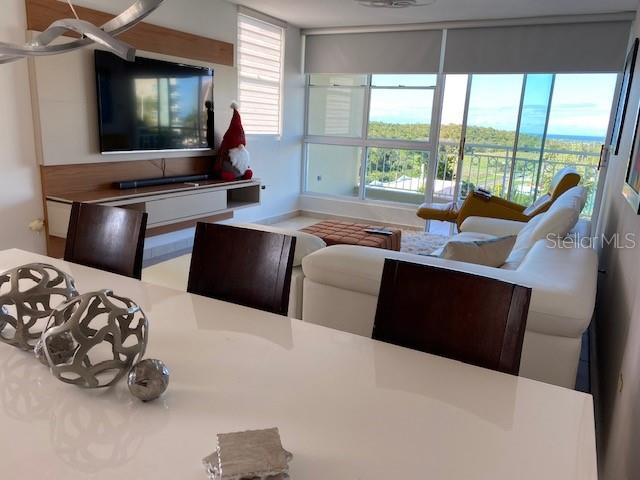 A modern living and dining area features a white sofa, television, and large windows — VISTA DEL MAR LUXURY BARRIO ARENALES ROAD 110 UNIT C 201, AGUADILLA, PR