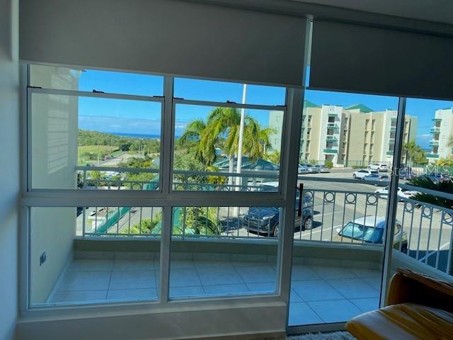 A view from a window looking out onto a balcony, parking lot, and distant hills — VISTA DEL MAR LUXURY BARRIO ARENALES ROAD 110 UNIT C 201, AGUADILLA, PR