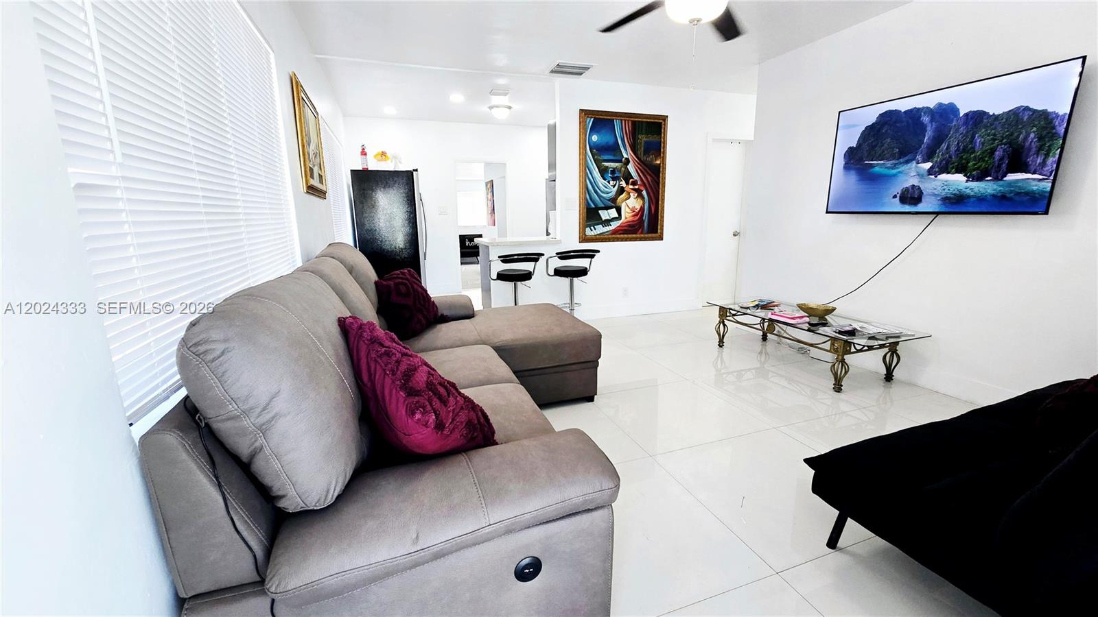 A living room features a gray sectional sofa, a wall-mounted television, and white tile flooring — 139 NW 14th Way, Dania Beach FL 33004, DANIA BEACH, FL