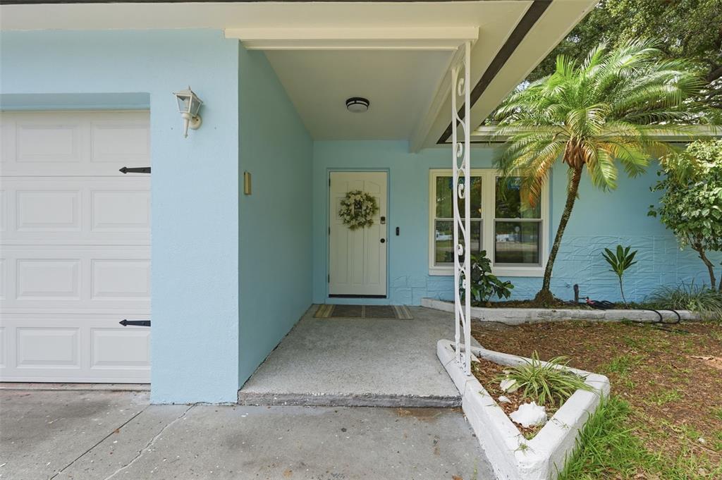 A light blue house exterior features a white front door, garage, and a palm tree — 2140 NE COACHMAN ROAD, CLEARWATER, FL