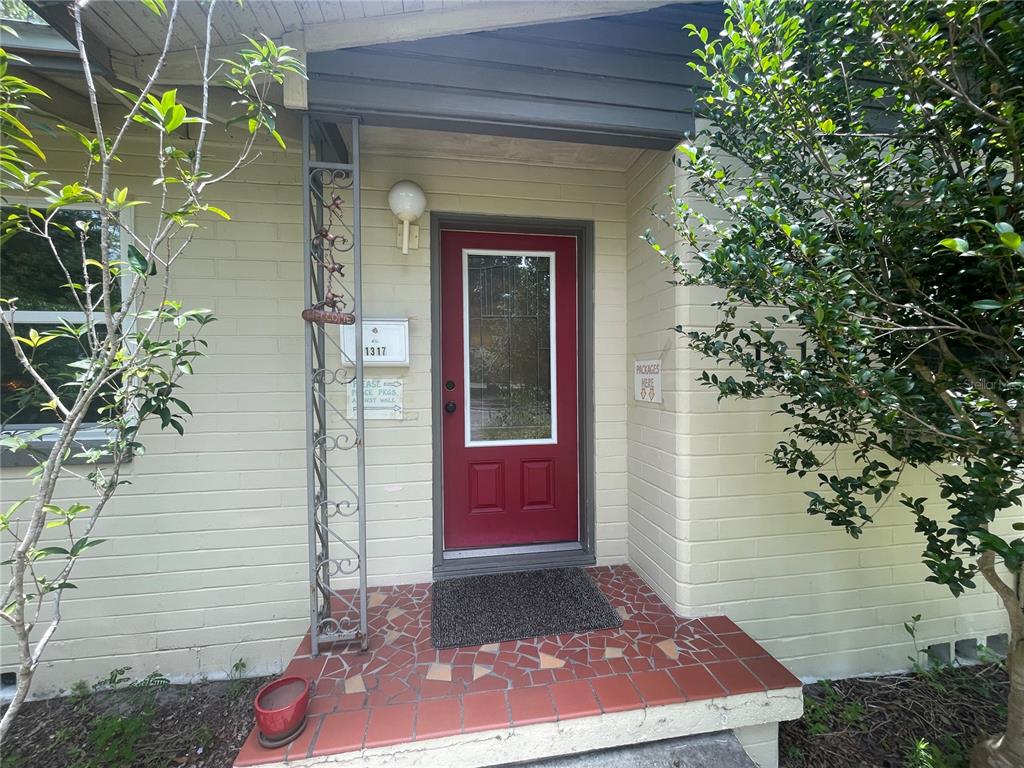 A red front door with a glass panel is set in a light-colored brick exterior — 1317 NW 4TH STREET, GAINESVILLE, FL