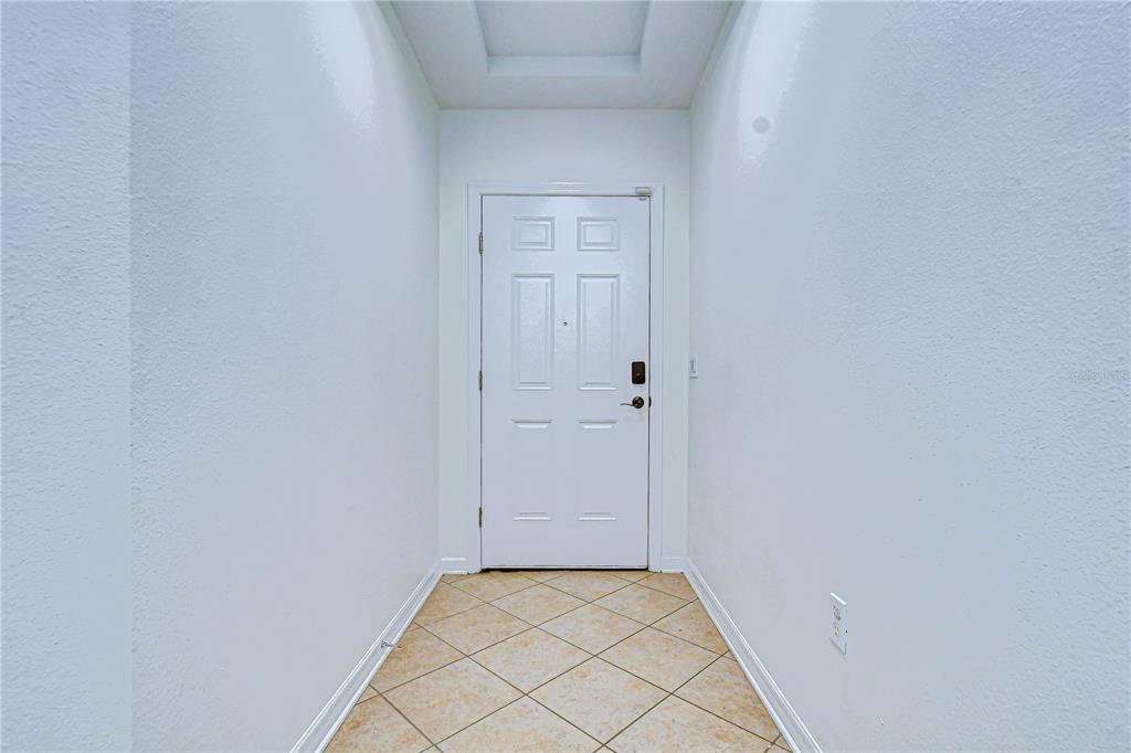A narrow entryway features white walls, a white front door, and light-colored tile flooring — 7809 TUSCANY WOODS DRIVE, TAMPA, FL