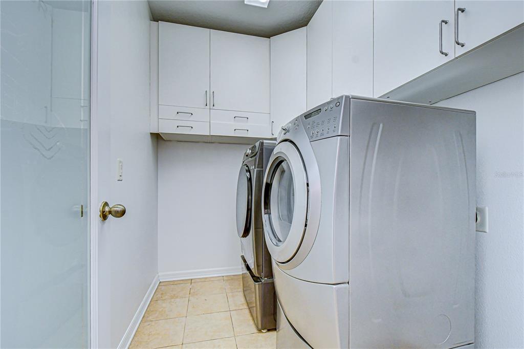 A laundry room features white cabinets, tile flooring, and a silver washer and dryer set — 7809 TUSCANY WOODS DRIVE, TAMPA, FL
