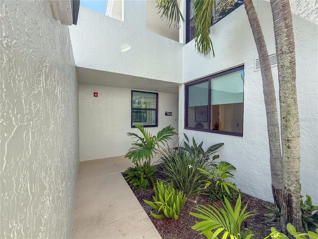 A walkway leads to the entrance of a white building with tropical landscaping — 806 BAYPORT WAY UNIT 806, LONGBOAT KEY, FL