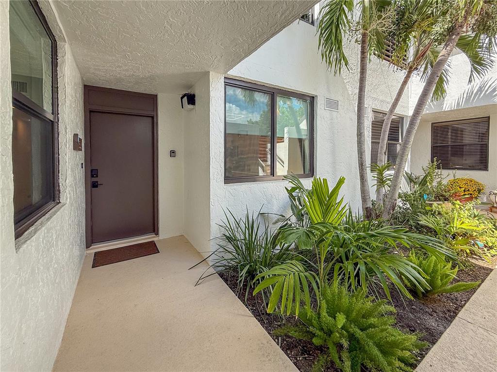 The exterior view shows a brown front door, a window, and landscaping by the entrance — 806 BAYPORT WAY UNIT 806, LONGBOAT KEY, FL