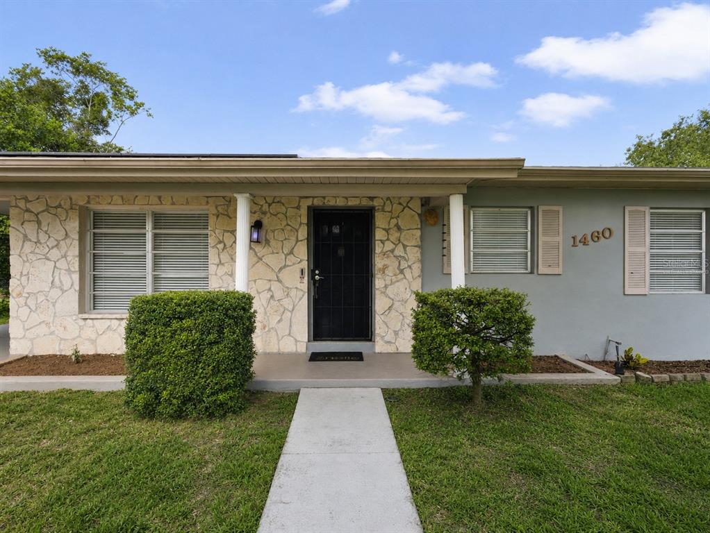 The exterior of a single-story house features a stone facade, a black front door, and shutters — 1460 E LOMBARDY DRIVE, DELTONA, FL