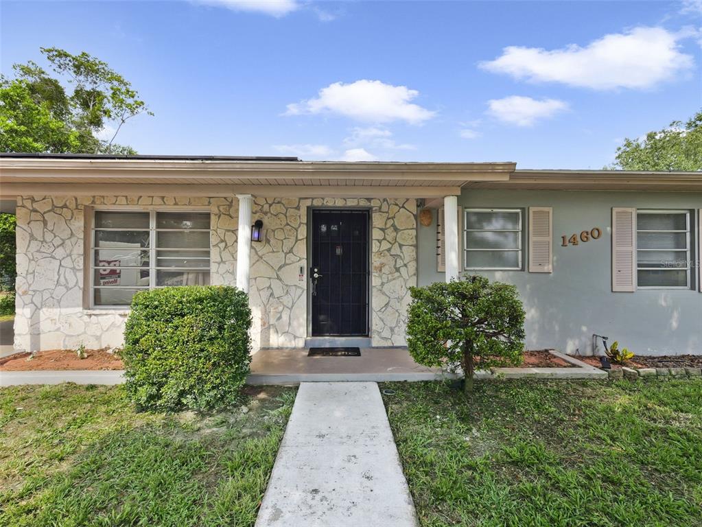 A single-story house exterior features a stone facade, a front door, and a concrete walkway — 1460 E LOMBARDY DRIVE, DELTONA, FL