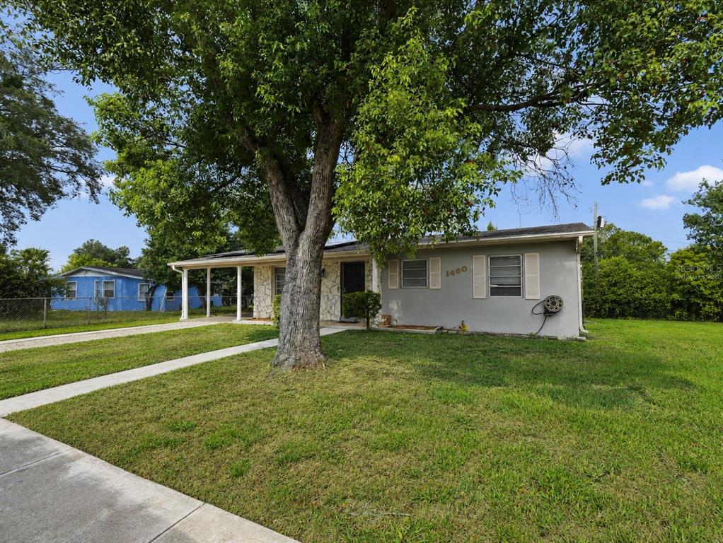 A single-story gray house with a stone facade, a large tree, and a covered porch — 1460 E LOMBARDY DRIVE, DELTONA, FL