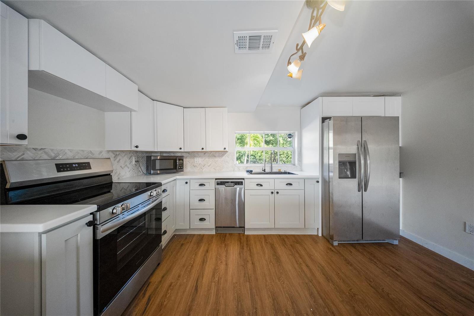 A kitchen features white cabinets, stainless steel appliances, a herringbone backsplash, and wood-look flooring — 133 Valois Boulevard, Key Largo FL 33037, KEY LARGO, FL