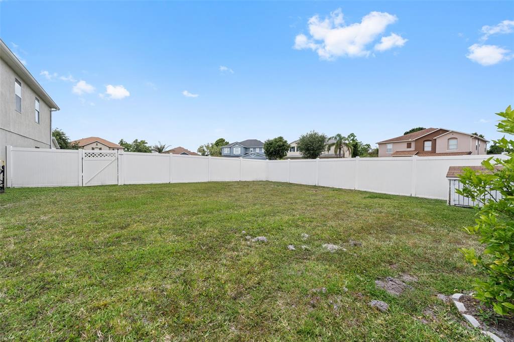 A grassy backyard is enclosed by a white vinyl fence under a vibrant sunset sky — 831 NEPTUNE POINTE LANE, KISSIMMEE, FL