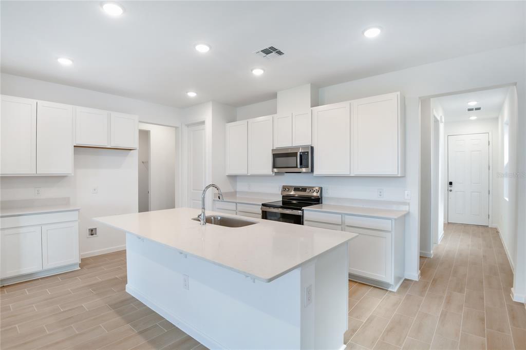A modern kitchen features white cabinets, a central island with a sink, and light-colored flooring — 6178 DAPHNE STREET, LAKE HAMILTON, FL