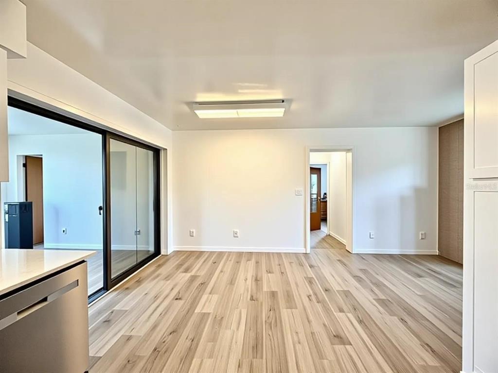 A bright, empty room features light wood-look flooring, white walls, a sliding glass door, and recessed lighting — 5235 SE 107TH STREET, BELLEVIEW, FL