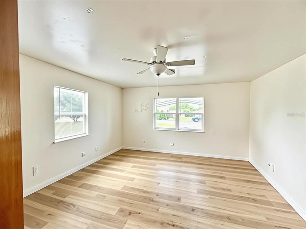 An empty room with light wood-look flooring, beige walls, and a ceiling fan — 5235 SE 107TH STREET, BELLEVIEW, FL