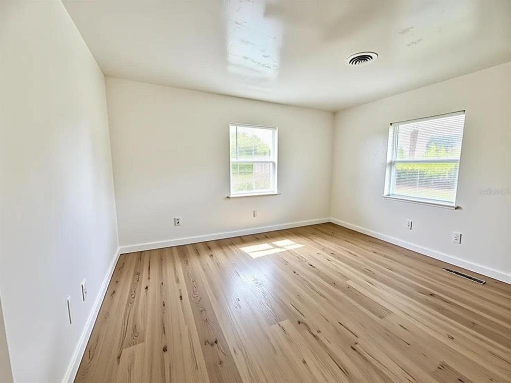 An empty room features light wood-look flooring, white walls, two windows, and a ceiling vent — 5235 SE 107TH STREET, BELLEVIEW, FL