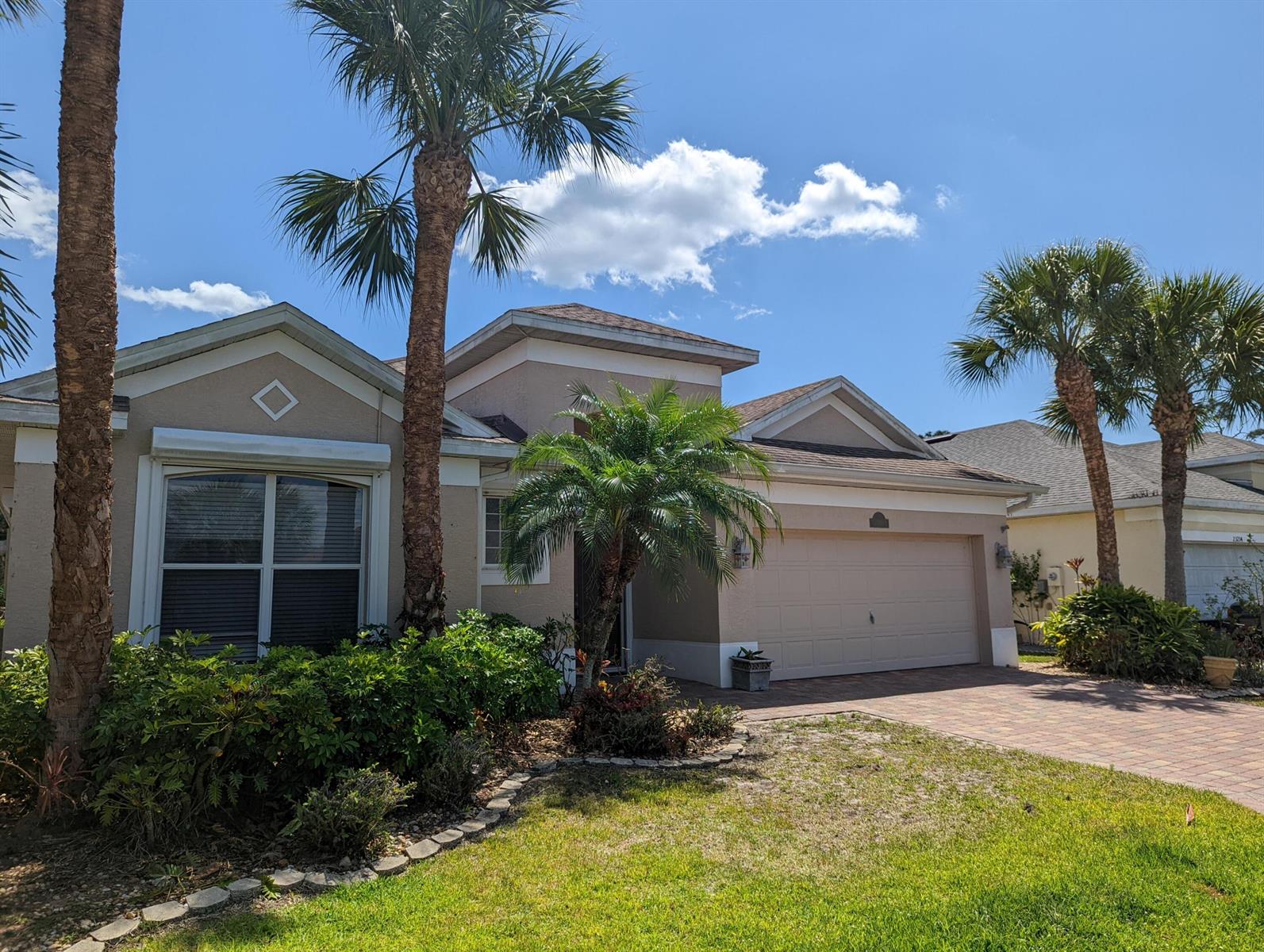 A beige single-story house with a two-car garage, palm trees, and a paved driveway — 23238 Marsh Landing Boulevard, FL 33928, FL