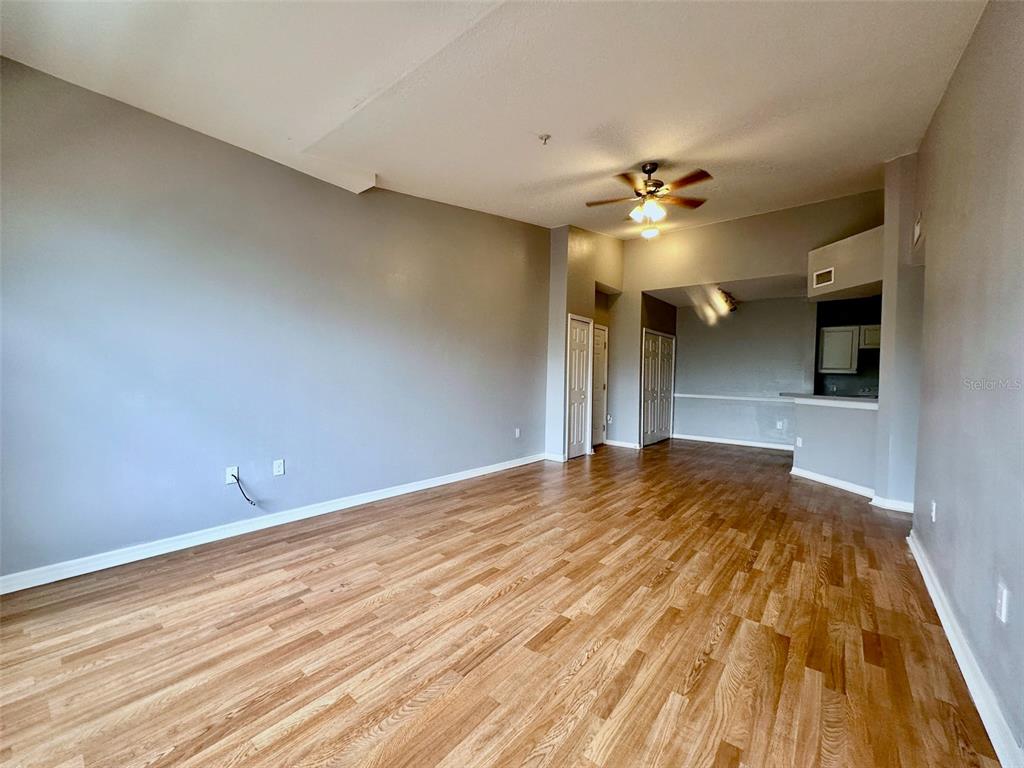 An empty living room features wood-look flooring, gray walls, and a ceiling fan — 5578 METROWEST BOULEVARD UNIT 1-302, ORLANDO, FL
