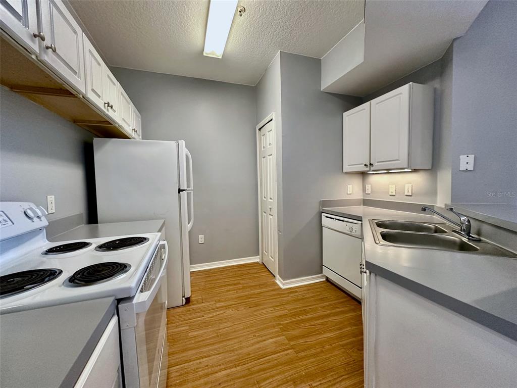 A kitchen features white cabinets, a white refrigerator, a white stove, and wood-look flooring — 5578 METROWEST BOULEVARD UNIT 1-302, ORLANDO, FL