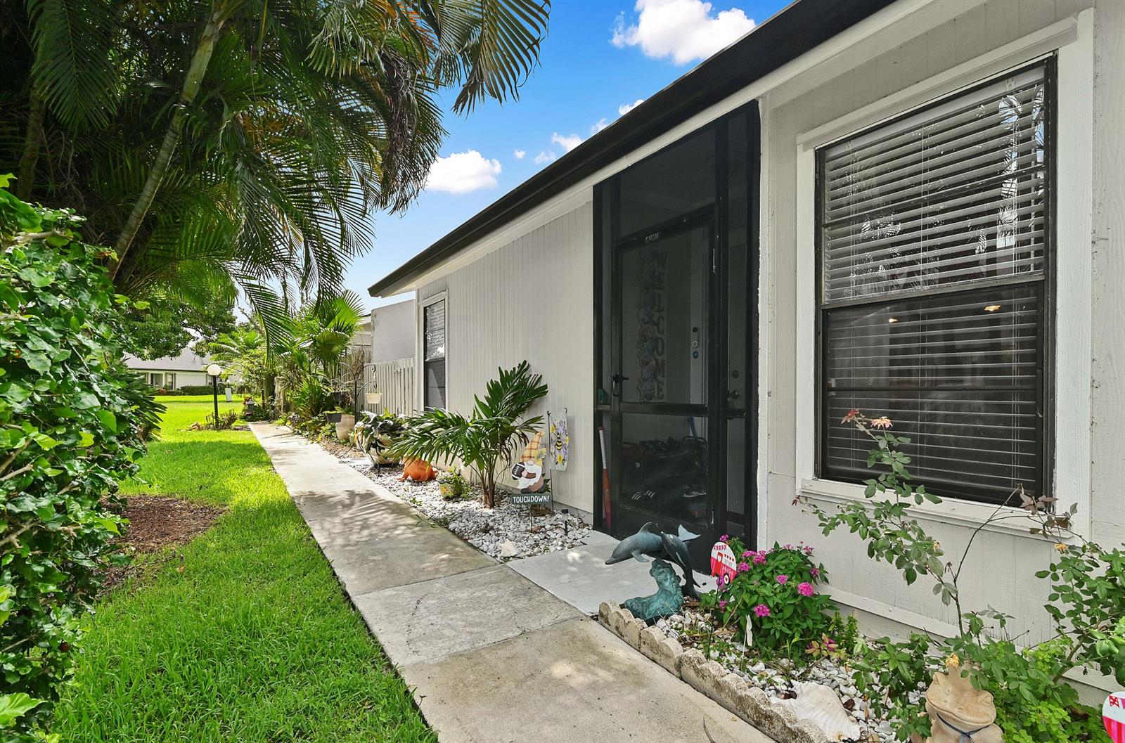 A side view of a house exterior featuring a walkway, landscaping, and a screen door — 4383 Willow Pond Circle, West Palm Beach FL 33417, WEST PALM BEACH, FL