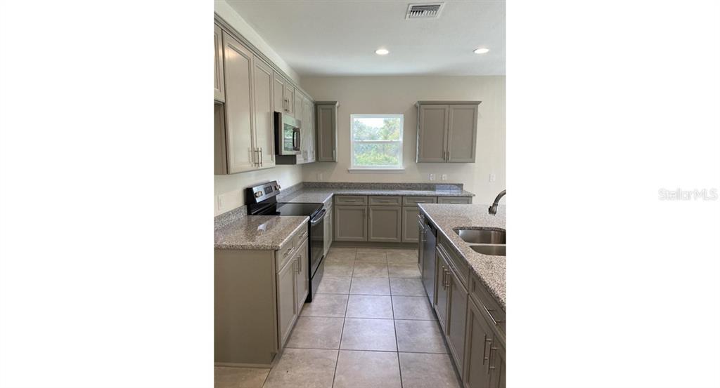 A kitchen features gray cabinets, granite countertops, stainless steel appliances, and tile flooring — 5961 GOTTFRIED LANE, NORTH PORT, FL