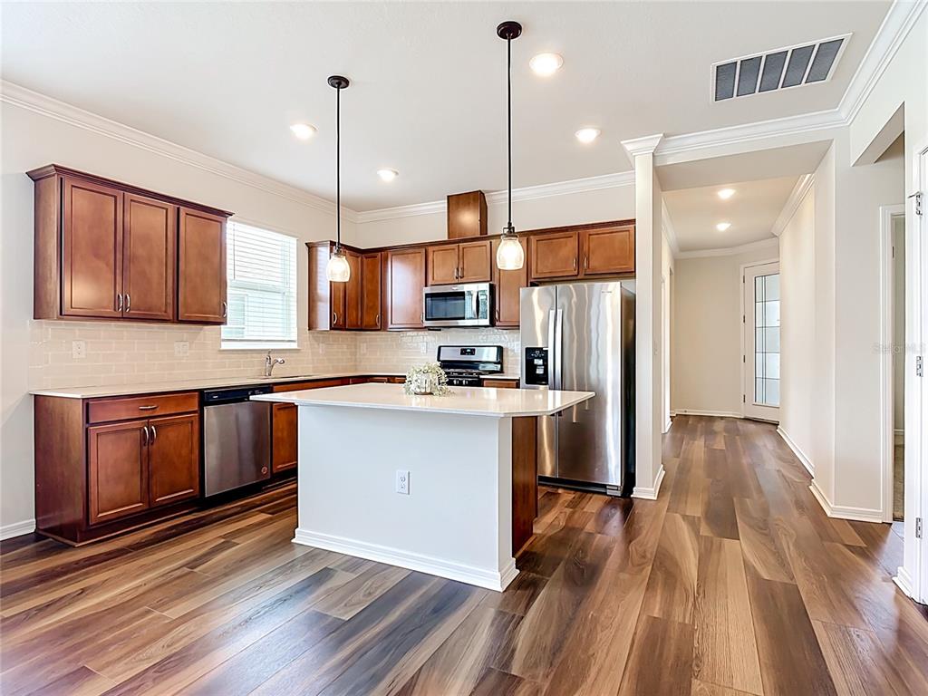 A kitchen with wood cabinets, stainless steel appliances, a white island, and wood-look flooring — 2949 CHERRY BLOSSOM LOOP, ST CLOUD, FL
