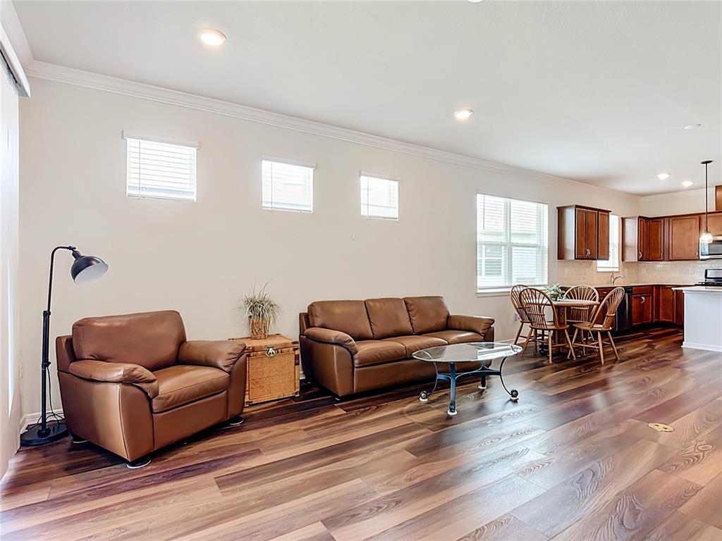 A living room with brown leather furniture, wood-look flooring, and an open kitchen — 2949 CHERRY BLOSSOM LOOP, ST CLOUD, FL