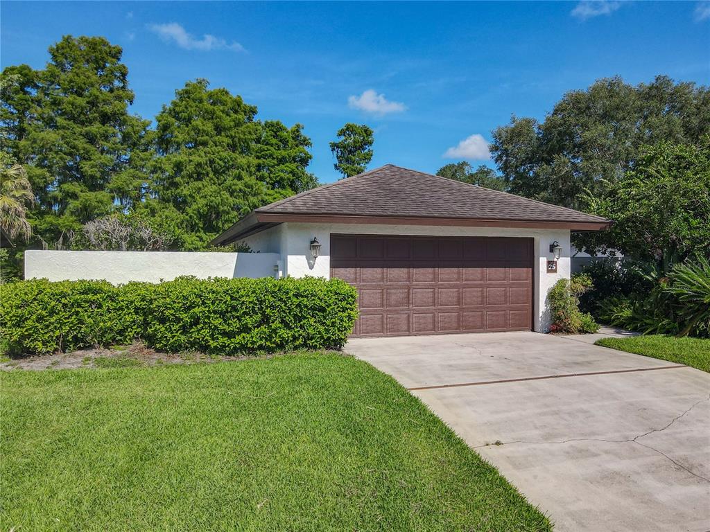 A detached garage with a brown door and a hip roof sits beside a hedge — 25 HUNTLEY COURT, HAINES CITY, FL