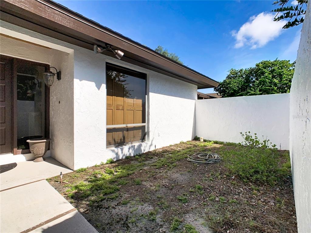 A white stucco house exterior features a front courtyard with a window and garden hose — 25 HUNTLEY COURT, HAINES CITY, FL