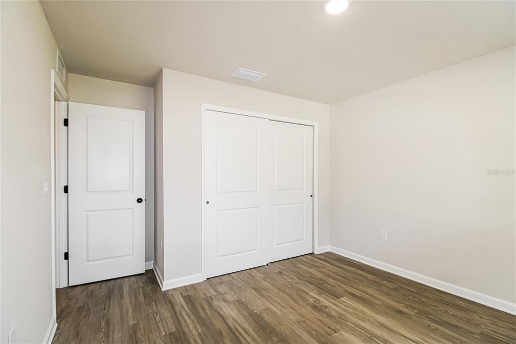 An empty bedroom features light-colored walls, wood-look flooring, a white door, and a sliding closet — 5953 W OAK PARK BOULEVARD, HOMOSASSA, FL