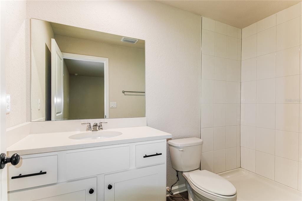 A bathroom features a white vanity with black hardware, a mirror, a toilet, and a shower — 5953 W OAK PARK BOULEVARD, HOMOSASSA, FL