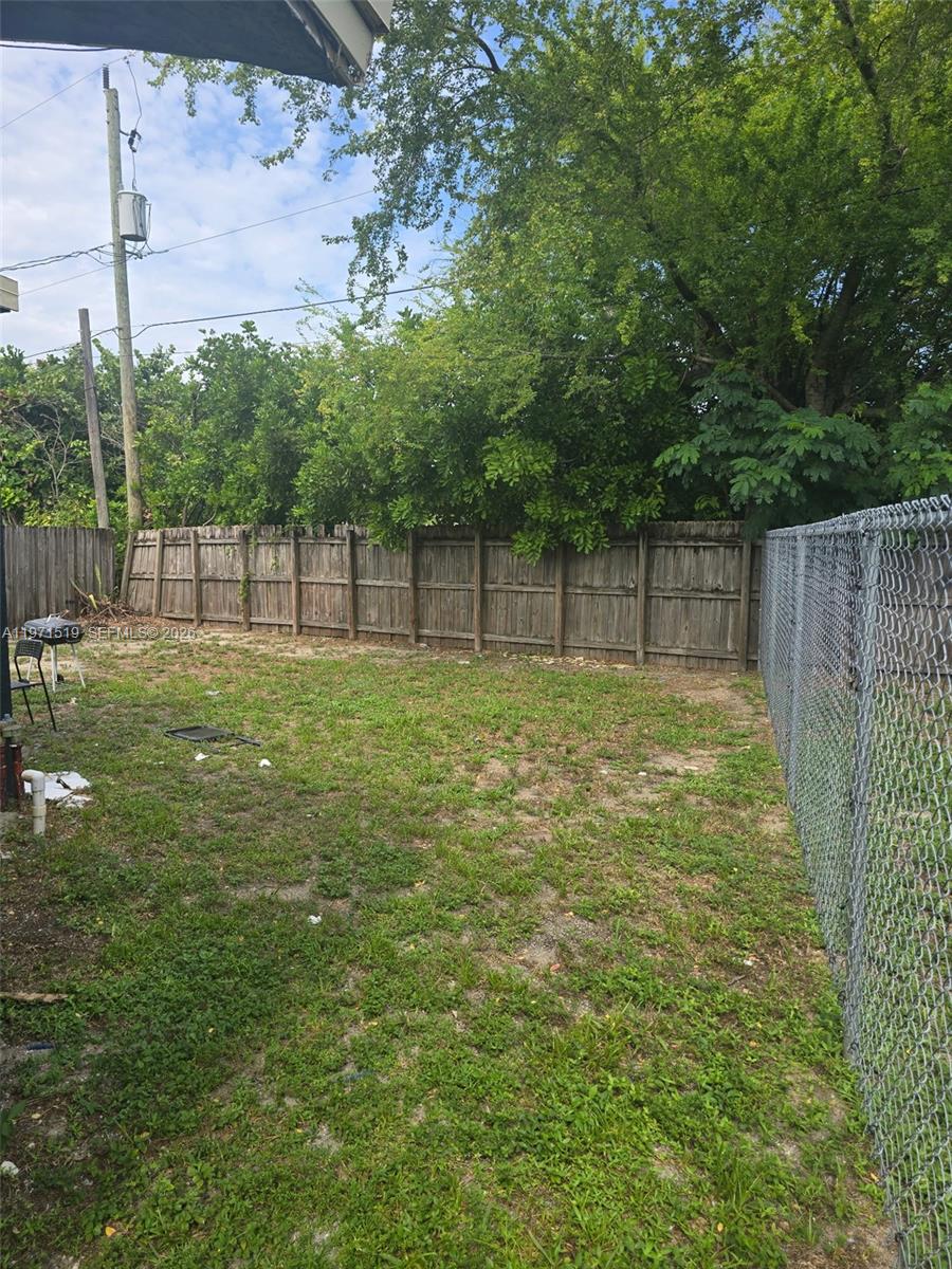 A fenced backyard features a patch of grass, scattered debris, and mature trees — 770 SW 2nd Ave, Deerfield Beach FL 33441, DEERFIELD BEACH, FL