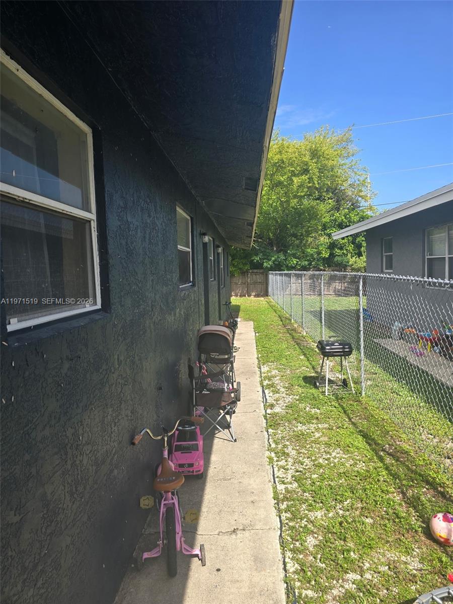 A narrow concrete walkway runs alongside a dark-painted exterior wall with a chain-link fence — 770 SW 2nd Ave, Deerfield Beach FL 33441, DEERFIELD BEACH, FL