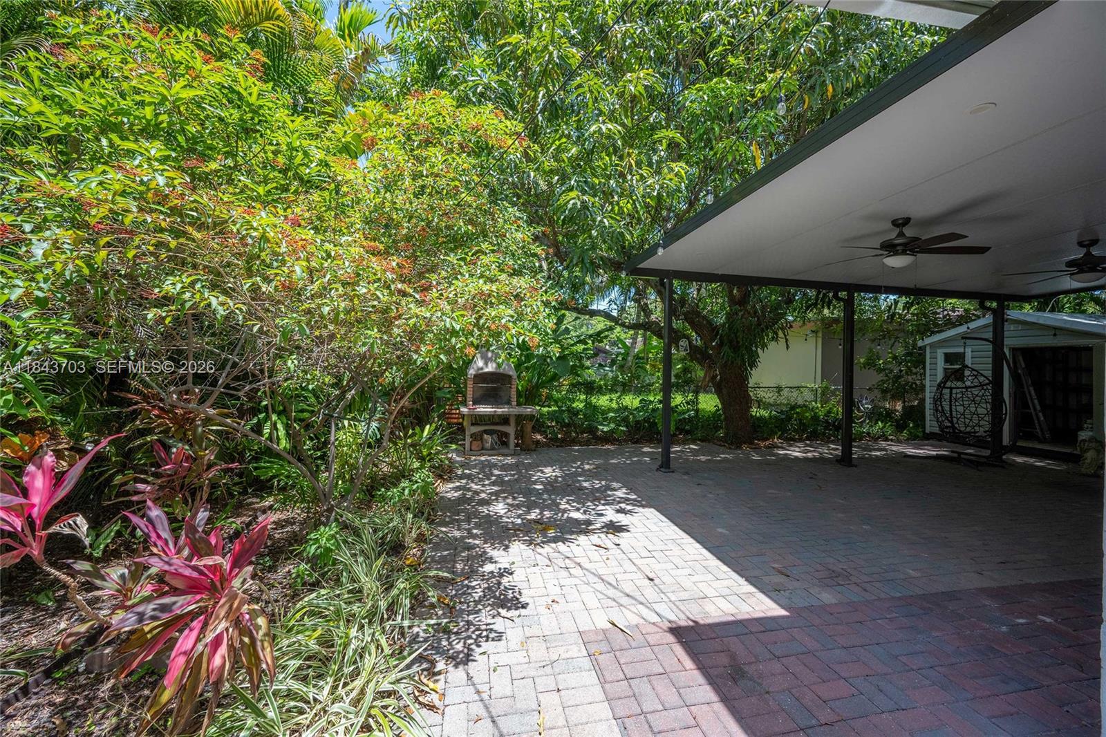 A paved patio area features a stone outdoor fireplace and a covered seating space — 13325 NE 10th Ave, North Miami FL 33161, NORTH MIAMI, FL