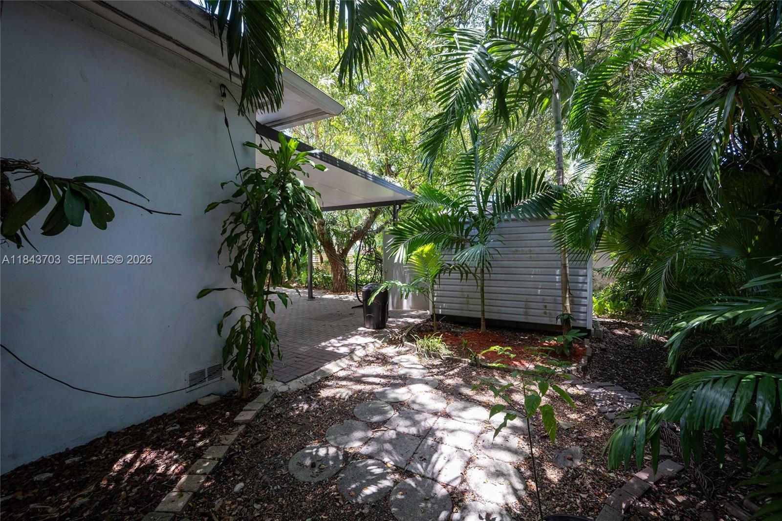 A backyard patio area features a paved walkway, a storage shed, and lush tropical landscaping — 13325 NE 10th Ave, North Miami FL 33161, NORTH MIAMI, FL