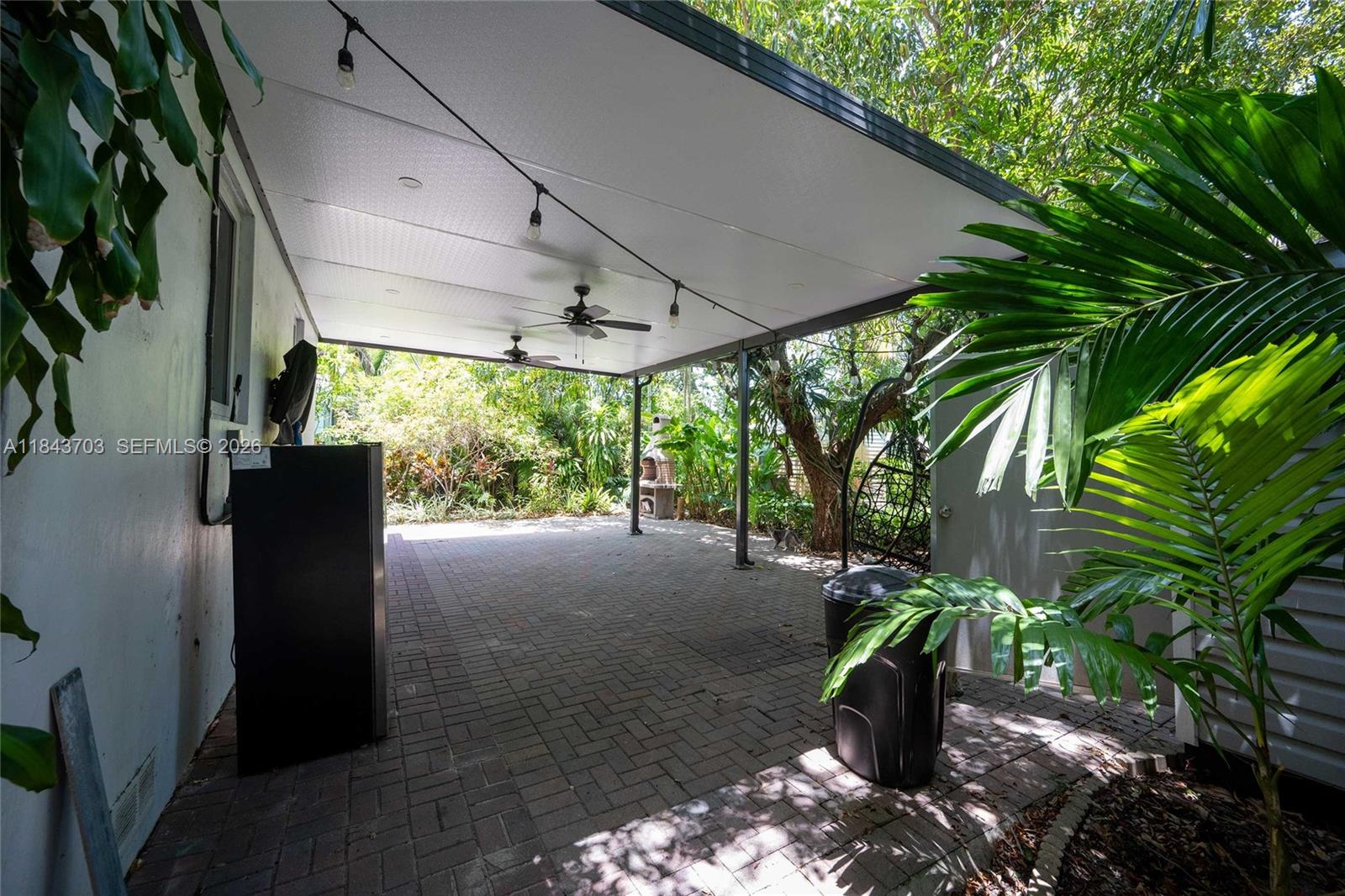 A covered patio features a brick floor, ceiling fans, string lights, and lush tropical landscaping — 13325 NE 10th Ave, North Miami FL 33161, NORTH MIAMI, FL