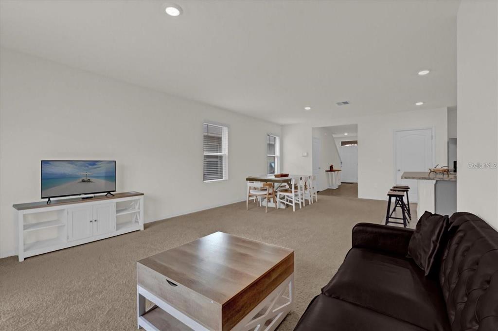 A living room with carpeted floors, a television on a white console, and a dining area — 1444 BERRY LANE, DAVENPORT, FL