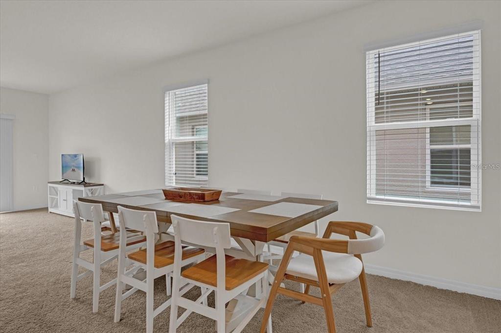 A dining area features a wooden table with chairs on carpeted flooring near two windows — 1444 BERRY LANE, DAVENPORT, FL