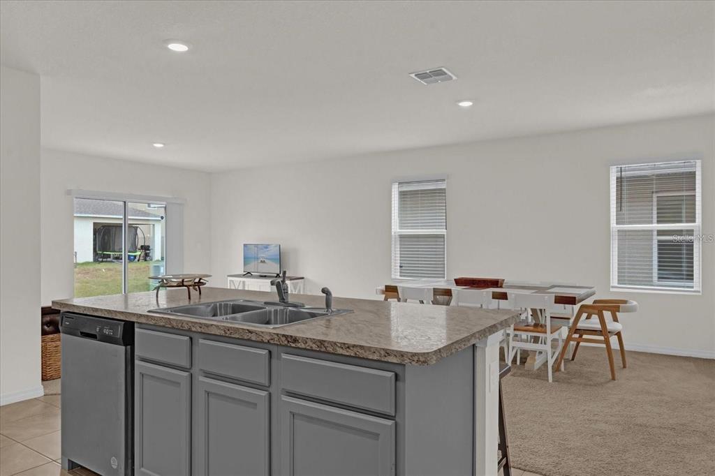 A kitchen island with a double sink and gray cabinets overlooks a dining area — 1444 BERRY LANE, DAVENPORT, FL