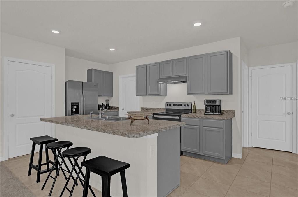 A kitchen features gray cabinets, a stone-look island with bar stools, and stainless steel appliances — 1444 BERRY LANE, DAVENPORT, FL