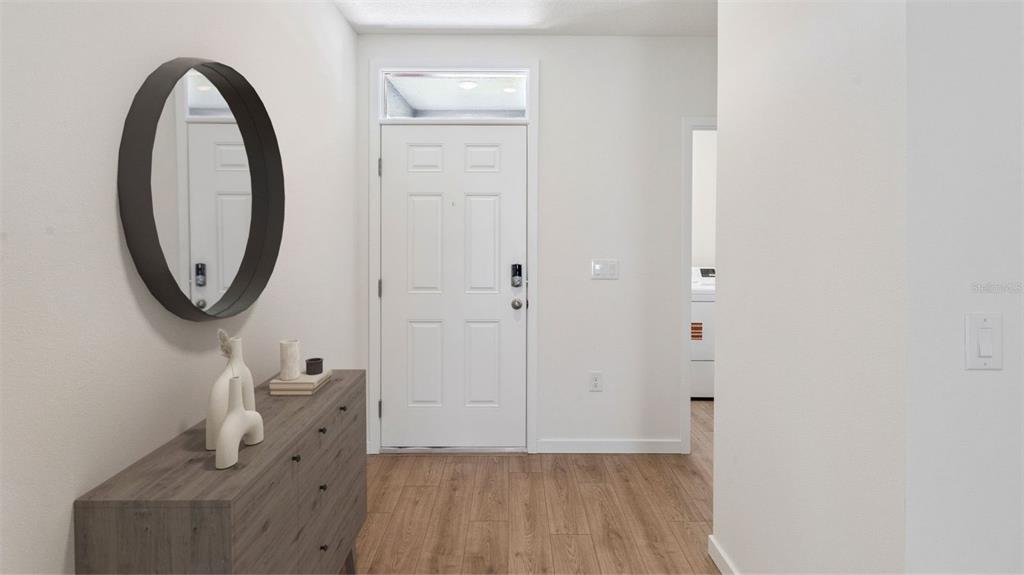 An entryway features a wood-look floor, a white front door, and a round wall mirror — 3061 HOUSE FINCH ROAD, ST CLOUD, FL