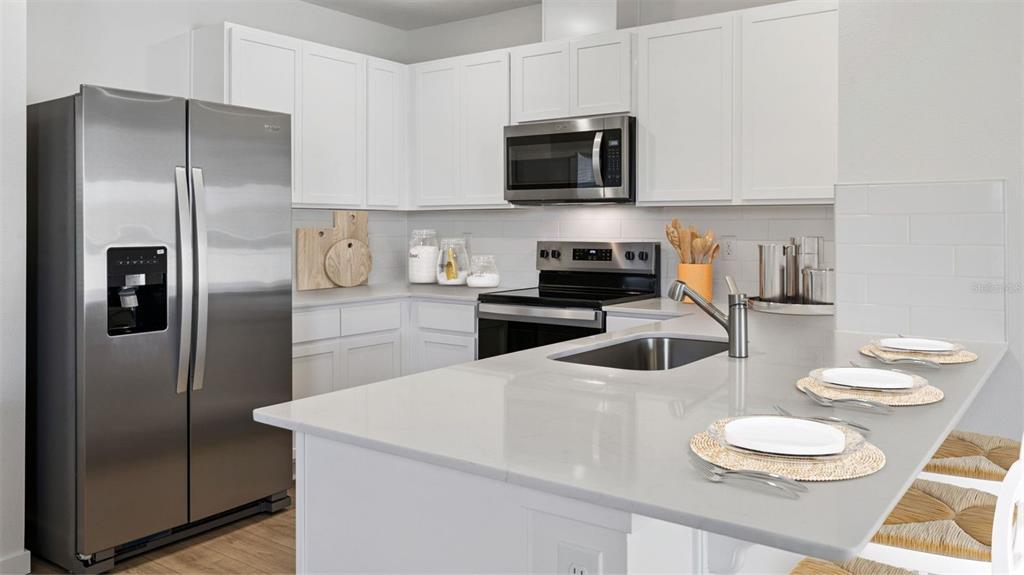 A modern kitchen features white cabinets, stainless steel appliances, and a quartz-topped island with seating — 3061 HOUSE FINCH ROAD, ST CLOUD, FL