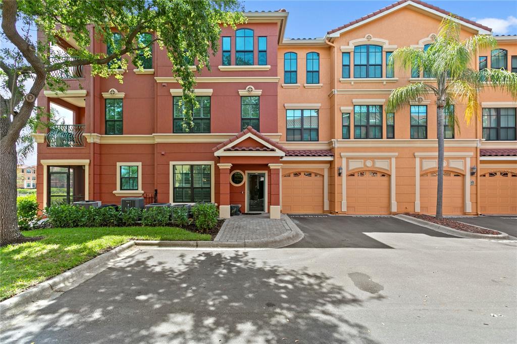 A multi-story townhouse complex with a red and orange facade, garages, and a paved entrance — 2741 VIA CIPRIANI UNIT 914A, CLEARWATER, FL