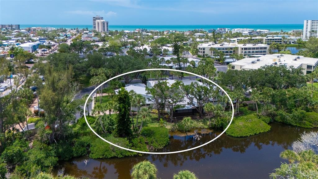 An aerial view shows a single-story house surrounded by trees and vegetation near a pond — 239 HOURGLASS WAY UNIT V7, SARASOTA, FL