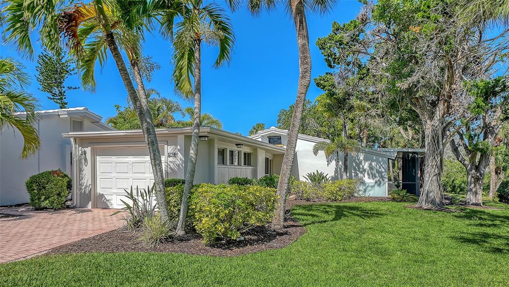 A white house with a garage and palm trees sits behind a green lawn — 239 HOURGLASS WAY UNIT V7, SARASOTA, FL