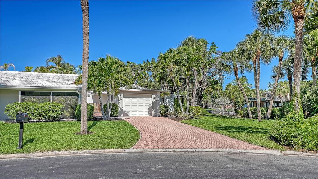 A single-story house with a white garage and a brick driveway surrounded by palm trees — 239 HOURGLASS WAY UNIT V7, SARASOTA, FL