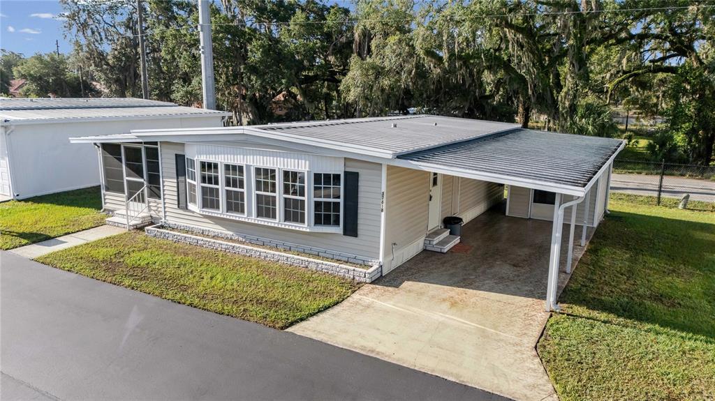 An exterior view of a single-story manufactured home with a carport and a metal roof — 37818 VALENCIA AVENUE, ZEPHYRHILLS, FL