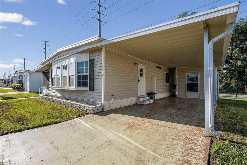 A single-story manufactured home features light-colored siding, a concrete carport, and a bay window — 37818 VALENCIA AVENUE, ZEPHYRHILLS, FL