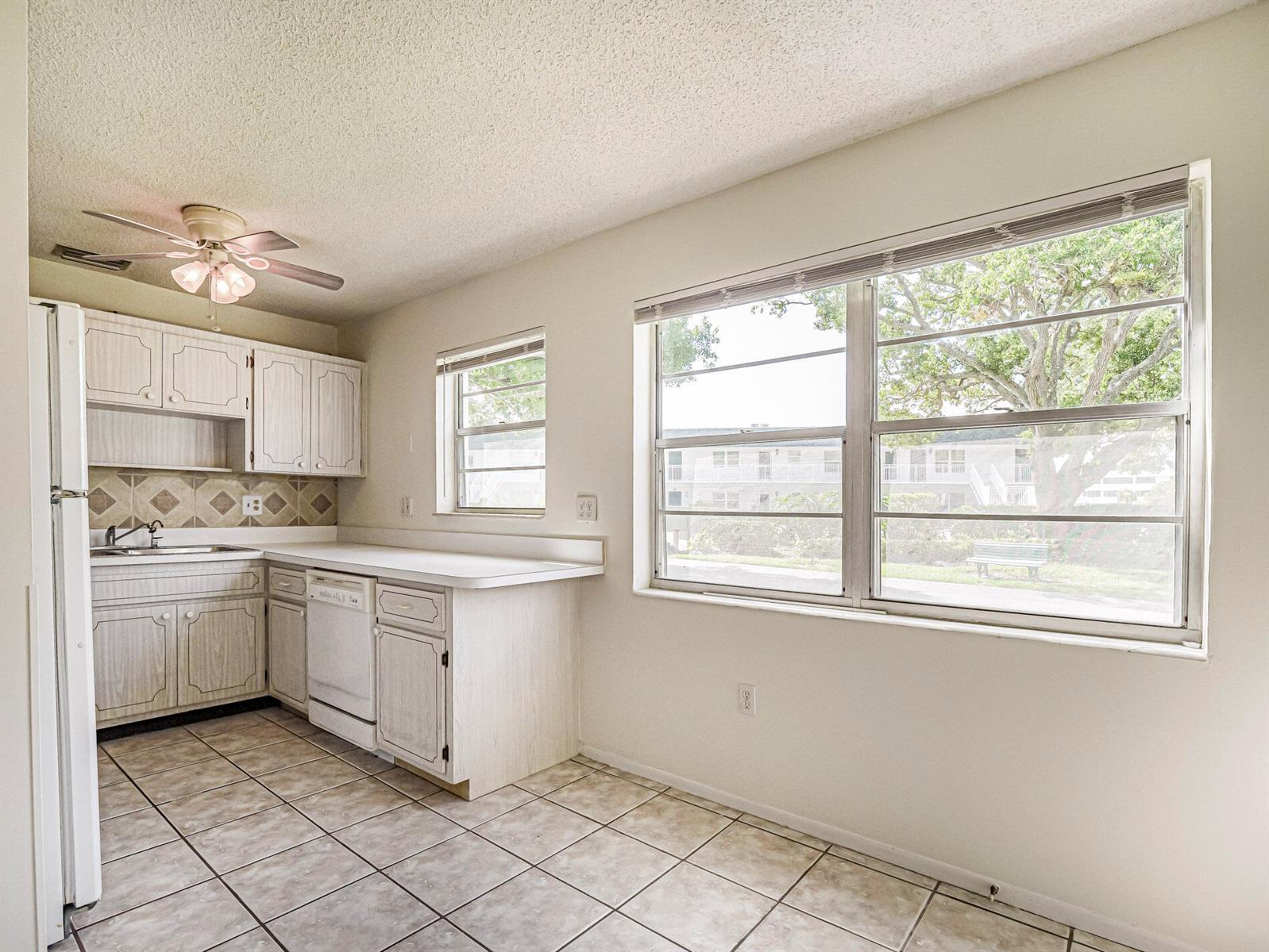 A kitchen with white cabinets, tile flooring, a dishwasher, and large windows overlooking trees — 2800 Indian River Boulevard, Vero Beach FL 32960, VERO BEACH, FL