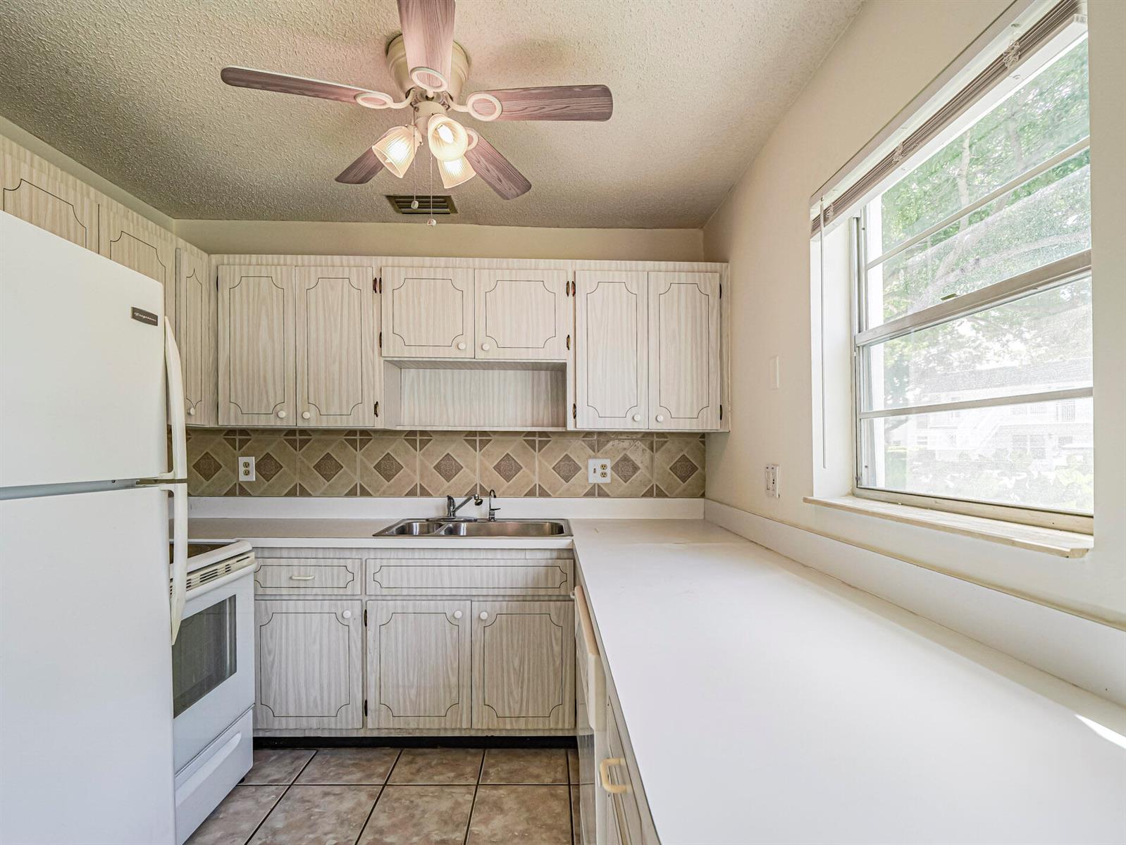 A kitchen features light wood-grain cabinets, white appliances, a tiled backsplash, and a ceiling fan — 2800 Indian River Boulevard, Vero Beach FL 32960, VERO BEACH, FL
