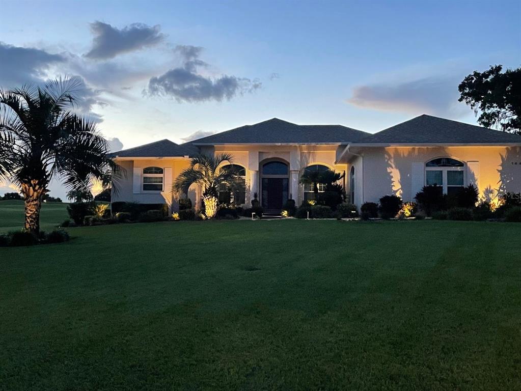 A single-story house with a large lawn and exterior lighting at dusk — 7042 MONTREAL DRIVE, LAKELAND, FL