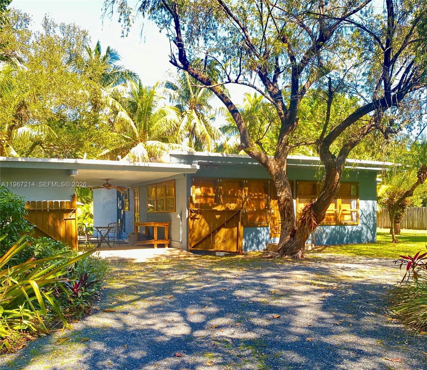 A single-story house with a gravel driveway, a covered patio, and mature trees — 5975 SW 60th St, South Miami FL 33143, SOUTH MIAMI, FL